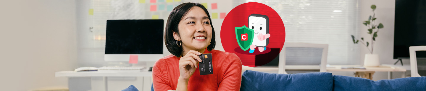 Seorang wanita tersenyum sambil memegang kad kredit di ruang pejabat rumah, dengan maskot Trust and Safety Carousell memegang perisai keselamatan hijau di sebelahnya.